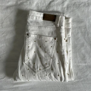 Vita jenas med guldprickar från Zara Woman - Säljer ett par vita jeans från Zara Woman med små guldprickar över hela byxan. Byxorna har klassisk femficksdesign, gylf med dragkedja och knapp samt raka ben. Perfekta för dig som vill sticka ut lite extra!