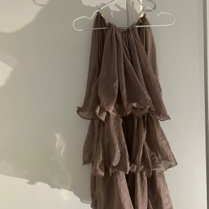 Brun glittrig volangklänning från Missguided - Supersöt brun klänning från Missguided med glittrigt tyg och flera lager volanger. Axelbandslös modell. Oanvänd 