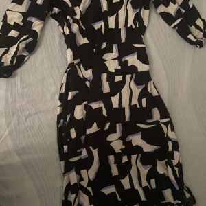 Snygg sommarklänning  - Säljer en långklänning med svart och vit bas samt inslag av ljuslila i ett grafiskt, abstrakt mönster. Klänningen har långa ärmar med lätt puff och en figurnära passform upptill. Perfekt inför kommande sommaren och så skönt material!