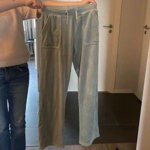 Ljusgröna velourbyxor från Juicy Couture - Säljer ett par ljusgröna velourbyxor från Juicy Couture med dragsko i midjan och stora fickor både fram och bak. Byxorna har en avslappnad passform och klassisk Juicy Couture-detalj på snöret. Perfekta för en chill och trendig look.