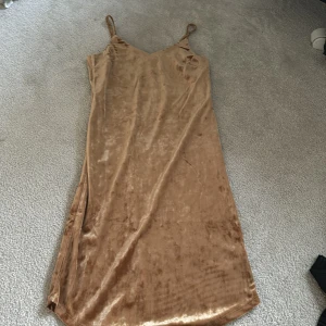 Champagnefärgad långklänning från XOXO Friends - Säljer en glansig och elegant långklänning i champagnefärg från XOXO Friends. Klänningen har smala axelband och en mjuk, följsam passform. Perfekt för dig som vill ha en stilren och trendig look.