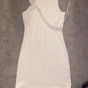 Vit ribbad oneshoulderklänning från H&M Divided - Säljer en vit ribbad oneshoulderklänning från H&M Divided. Klänningen har snörningsdetalj längs axeln och är tillverkad i stretchigt material. Perfekt för dig som gillar trendiga och stilrena plagg.