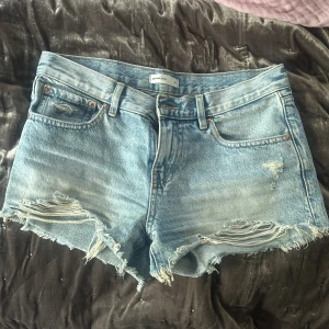 Ljusblå jeansshorts med fransar från Perfect Jeans - Säljer ett par ljusblå jeansshorts från Perfect Jeans. De har råa fransade kanter och slitna detaljer framtill. Klassisk femficksmodell med normal passform och bälteshällor. Perfekta för varma dagar!