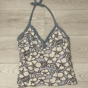 Blommig halterneck linnetopp - Säljer en blommig halterneck linnetopp från Roxy i blått och vitt. Toppen har v-ringning och knyts i nacken. Perfekt för varma dagar och har ett stort blommönster över hela plagget. Storlek 36/38 men är ganska liten i storleken💕