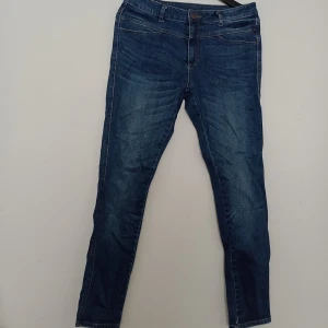Blå skinny jeans - Säljer ett par klassiska blå skinny jeans från Flash Jeans, modell Bonnie. Jeansen har fem fickor, snygga sömmar och en liten blomdetalj på niten. Tillverkade i bomull med lite stretch för extra komfort.