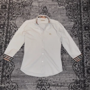Vit skjorta Burberry - Säljer en vit skjorta från Burberry. Jag har knappt använt den, just nu är den bara i min garderob så därför vill jag sälja den. Det står storlek M i skjortan men den är i liten passform så jag säljer den som S/XS.  Perfekt för en stilren look.