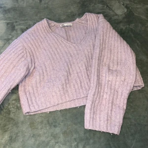 Ljuslila ribbad tröja från Zara  - Säljer en ljuslila stickad tröja från Zara. Tröjan är croppad, har v-ringning och är ribbstickad med långa ärmar. Perfekt för lager-på-lager och en mysig vardagslook. Hög kvalitet och inga tecken på användning. Den passar bra med många olika typer av kläder 