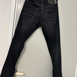 Svarta jeans från Jack & Jones - Säljer ett par svarta jeans från Jack & Jones med slitna detaljer och raka ben. Jeansen har fem fickor och klassisk knappgylf. Perfekta för en avslappnad stil.