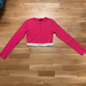 Rosa croppad långärmad topp från FB Sister - Säljer en rosa croppad långärmad topp från FB Sister. Toppen har en vit elastisk kant nertill med texten 'originals' och är tillverkad i mjukt bomullsmaterial. Perfekt för en trendig och sportig look. (Finns matchande byxor)