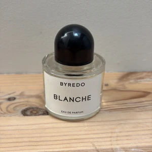 Byredo Blanche Eau de Parfum - Byredo Blanche Eau de Parfum i en stilren, rund glasflaska med svart rund kork och vit etikett. Doften är känd för sin fräscha och rena karaktär, perfekt för dig som gillar minimalistisk design och exklusiva parfymer. Parfymen är helt oanvänd och priset kan diskuteras. Nypris, 1700 kr. 