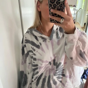 Oversized hoodie med batikmönster - Säljer en oversized hoodie med batikmönster i svart, grått och ljuslila. Tröjan har långa ärmar, huva och är croppad i modellen. Perfekt för en avslappnad och trendig stil.