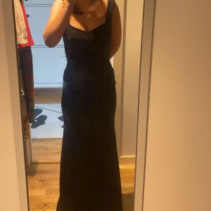 Svart långklänning med öppen rygg - Säljer en elegant svart långklänning med smala axelband och öppen rygg. Klänningen har en tight passform och är perfekt för festliga tillfällen. Materialet är mjukt och följsamt, vilket ger en snygg siluett.