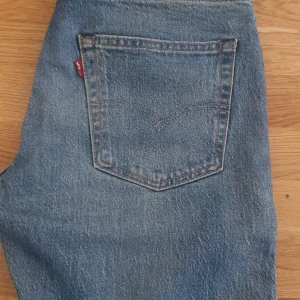 Levis jeansbyxor i klassisk blå denim - Klassiska blå Levis jeans med rak passform och femficksdesign. Byxorna har en tydlig Levis-logga på bakfickan och är tillverkade i slitstark denim. Perfekta för en avslappnad och tidlös stil.