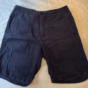Mörkblå shorts från NN07 - Snygga mörkblå shorts från NN07 med elastisk midja och snörning. Shortsen har sidofickor fram och bakfickor, varav en med knapp. Tillverkade i ett mjukt tyg som känns bekvämt mot huden.