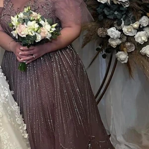 Glittrig lila långklänning med tyllärmar - Säljer en magisk lila långklänning med glittriga detaljer och puffiga tyllärmar. Klänningen har v-ringning och markerad midja, perfekt för bal eller fest. Materialet är lätt och skimrande, vilket ger en lyxig känsla.