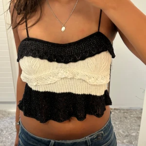 Svart och vit stickad croppad linnetopp - Säljer en stickad croppad linnetopp i svart och vitt med volangkant nertill. Toppen har smala axelband och ett fint mönster i stickningen. Perfekt för sommaren och passar till både jeans och kjol.