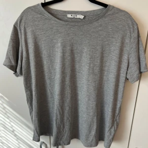 Grå t-shirt från NA-KD - En enkel och stilren grå t-shirt från NA-KD. T-shirten har rund halsringning och korta ärmar. Perfekt basplagg att matcha med olika outfits.