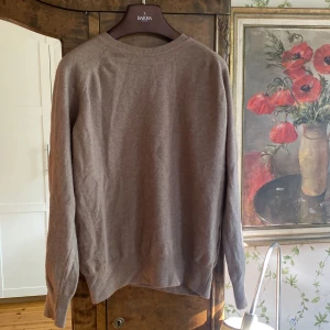 Oscar Jacobson tröja - Säljer en klassisk beige stickad tröja från Oscar Jacobson. Tröjan har rund halsringning och långa ärmar med ribbade muddar. Tillverkad i Italien och passar perfekt för lager-på-lager under kyliga dagar. Trevlig på sommarkvällen. 