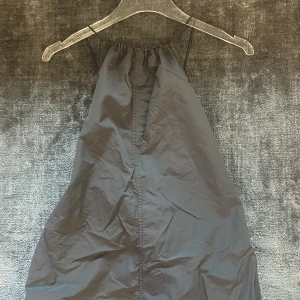 Grå halterneckklänning med dragsko - Säljer en grå halterneckklänning med smala axelband och dragsko i midjan. Klänningen har en enkel och stilren design i ett lätt och syntetiskt material, perfekt för varma dagar. Ifrån Zara 
