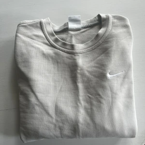 Ljusgrå sweatshirt från Nike - Säljer en ljusgrå sweatshirt från Nike med klassisk rund hals och broderad vit logga på bröstet. Tröjan är i mjuk bomull och har en enkel, stilren design som passar till det mesta. 7/10 i skick pga ett litet litet hål (se bild 4) Passar både S och lite mindre M.