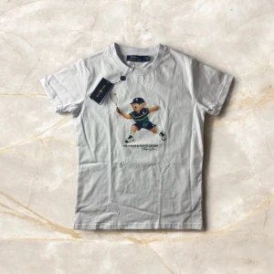 Ralph Lauren Polo Bear T -shirt - Säljer en vit Ralph Lauren T-shirt med det ikoniska Polo Bear-motivet där nallen spelar tennis – en riktig samlarfavorit! T-shirten är i storlek M och kommer helt ny med tagg kvar.  🔹 Detaljer: ✔ Färg: Vit ✔ Storlek: S ✔ Modell: Passar både herr och dam (unisex) ✔ Motiv: Polo Bear by Ralph Lauren – Tennis edition ✔ Skick: Ny med tagg – aldrig använd ✔ Material: Mjuk och bekväm bomull  En trendig och charmig t-shirt som drar blickarna till sig – perfekt till både jeans och shorts.  📦 Kan