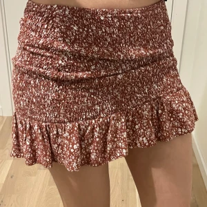 Brun/röd blommig volangkjol från Mango - Supersöt kort kjol från Mango i röd brun färg med vitt blommönster. Kjolen har smockad midja och volang nertill som ger en fin look. Perfekt att styla med en enkel topp då den passar till allt💕skriv gärna för frågor och tryck ej på köp nu innan ni kontaktar! Storlek: XS men mycket stretchig 