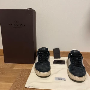 Valentino Garavani sneakers i Mörk blå mocka - Säljer ett par svarta sneakers från Valentino Garavani i mocka. Dustbag, box och kuvert medföljer. Skorna har en defekt vid sulan. Om du har en fråga eller om du undrar nåt om tex sulan så bara fråga 
