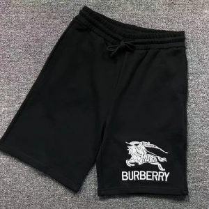Svarta shorts från Burberry med logga - Svarta shorts från Burberry med vit broderad logga och motiv på ena benet. De har elastisk midja med snörning och avslappnad passform. Perfekta för en stilren och bekväm look.