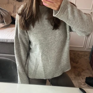 Grå stickad tröja med vid ärm - Mysig grå stickad tröja med rund hals och långa vida ärmar. Tröjan har en enkel och clean design med ribbade muddar vid ärmslut och nederkant. Lite nopprig men går enkelt att ta bort