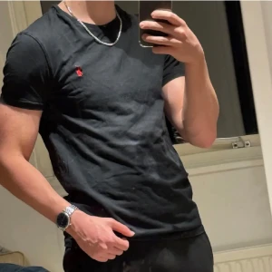 Svart t-shirt från Polo Ralph Lauren - Svart slim fit t-shirt från Polo Ralph Lauren med klassisk röd logga broderad på bröstet. Modellen har rund hals och korta ärmar, tillverkad i mjuk bomull som sitter skönt mot kroppen. 