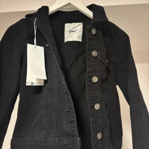 Svart jeansjacka från ONLY XS - Svart jeansjacka från ONLY i storlek XS. Klassisk modell med krage, silverfärgade knappar framtill och långa ärmar. Snygg och enkel att matcha med allt, perfekt för dig som gillar en clean och cool stil. Helt ny med prislapp kvar!