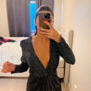 Svart glittrig kortklänning med djup v-ringning - Supersnygg svart kortklänning med glittriga prickar och djup v-ringning.