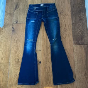 Blå bootcut jeans med slitningar - Snygga jeans från Gina 14+ i färgen mörkblå. Perfekt till en avslappnad cool look. Knappar på sidan av byxorna. Används endast två gånger.