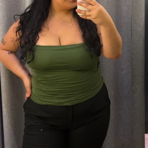 Olivgrön bandeau tubtopp - Säljer en olivgrön bandeau tubtopp med stilren och enkel design. Toppen är axelbandslös och sitter tight mot kroppen, perfekt för dig som gillar minimalistiska och trendiga plagg. Materialet känns mjukt och stretchigt, vilket gör den bekväm att bära hela dagen.