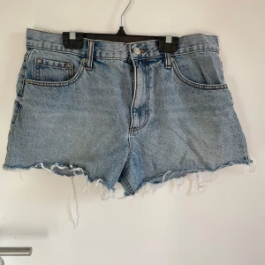 Blå jeansshorts från ASOS DESIGN - Snygga blå jeansshorts från ASOS DESIGN med hög midja och rå, fransig kant. Klassisk femficksmodell med knapp och dragkedja framtill. Perfekt passform enligt mig!! Säljes då dom inte passar längre.