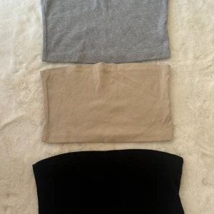 3-pack ribbade tubtoppar från SHEIN - Säljer ett 3-pack tubtoppar från SHEIN i storlek L. Färgerna är svart, beige och grå. Alla topparna är ribbade och har bandeau-modell, perfekta för att styla med jeans eller kjol. Materialet är mjuk och stretchig polyester som sitter skönt mot kroppen.