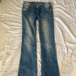Lågmidjade bootcut jeans från Redseventy - Säljer dessa supersnygga blå jeans från Redseventy med coola bakfickor med vingar. Tyvärr har jeansen lite defekter, de har slitningar mellan benen där jag lagat ett hål tidigare. Tyget runt knappen börjar även bli lite slitet men båda defekter går enkelt att laga😊Mått: 39cm i midjan och 82cm i innerbenslängd💗💗