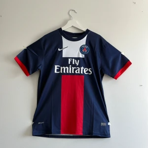 PSG Ibrahimović tröja Nike M - Paris Saint-Germain matchtröja med Ibrahimović och nummer 10 på ryggen. Snygg marinblå färg med röd vertikal panel och vita detaljer. Kortärmad, tillverkad i lätt Dri-FIT material som andas. PSG-emblem och Nike-logga på bröstet, Fly Emirates tryck framtill.
