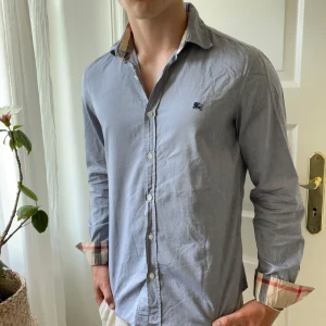 Burberry skjorta Grå / blå - Väldigt snygg färg, grå / blå. Storlek M och modellen är 180,75 kg. Inga defekter förutom en liten fläck som ni ser på sista bilden på högra bröstet. 