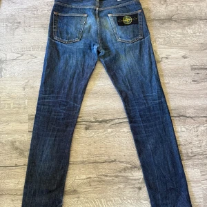 Stone Island blå jeans W28 L34 - Snygga blå jeans från Stone Island med klassisk patch på bakfickan och tydliga kontrastsömmar. Jeansen har rak passform och är tillverkade i slitstarkt denim med cool tvättad look. Perfekta för dig som gillar streetwear och vill sticka ut lite extra.