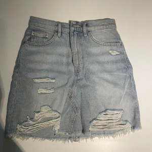 Ljusblå jeanskjol  - Säljer en ljusblå jeanskjol från DIVIDED i storlek 36. Kjolen har slitna detaljer, fransad nederkant och klassiska fickor både fram och bak. 