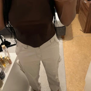 Beige cargopants med fickor - Säljer ett par beige cargopants med flera praktiska fickor på sidorna. Byxorna har en relaxed passform och är tillverkade i ett mjukt bomullsmaterial. Perfekt för dig som gillar streetstyle och vill ha en cool och avslappnad look.