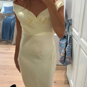 Champagnefärgad långklänning med slits - Säljer en elegant långklänning  med offshoulder och v-ringad överdel. Klänningen har öppen rygg och en snygg slits framtill. Materialet är mjukt och har en lätt glans,  jag är 170 och den släpar i marken för mig 