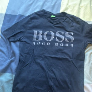 Svart Hugo Boss t-shirt med tryck - Snygg svart t-shirt från Hugo Boss med stort BOSS-tryck i vitt på bröstet. Klassisk rund hals och korta ärmar. Perfekt för dig som gillar stilrena märkesplagg och vill ha en enkel men cool look.