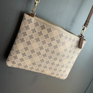 Rutig beige axelväska från By Malene Birger - Snygg axelväska från By Malene Birger i beige och grått med rutigt mönster och guldfärgad dragkedja. Väskan har en stilren, rektangulär form och justerbar axelrem i brunt skinn. I gott skick! Inga skador🌸