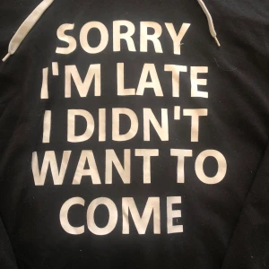 Svart hoodie med vit text och snörning - Svart hoodie med vit snörning i huvan och stor vit text på framsidan: 'SORRY I'M LATE I DIDN'T WANT TO COME'. Tröjan har lång ärm och klassisk passform, perfekt för chill dagar. 