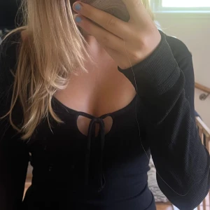 Svart ribbad långärmad topp Bik Bok - Svart långärmad topp från Bik Bok med ribbad struktur och snygg knytning framtill vid urringningen. Modellen är offshoulder och har en croppad passform som ger en trendig vibe. Perfekt för dig som gillar stilrena och coola plagg.