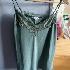Grön linnetopp med spets från Amisu/new yorker - Snygg ljusgrön linnetopp från Amisu/new yorker med tunna axelband och vacker spetsdetalj längs v-ringad halsringning. Storleken är L men passar även mig som är S/xs, det ända är att den kan var lite lång. Annars kan man justera via axelbanden. Använt fåtal gånger och säljer pga att jag knappt använder den!!