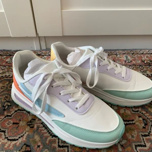 Pastellfärgade sneakers - Snygga sneakers i pastellfärger med vit bas, ljuslila, mintgrön, ljusblå, orange och gul. Skorna har snörning och platt sula med mintgrönt mönster undertill. Perfekt för dig som gillar färg och vill sticka ut med din stil.