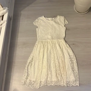 Vit spetsklänning från Ellos - Superfin vit kortklänning från Ellos med blommigt spetsmönster och rund hals. Klänningen har korta ärmar och ett lätt utställt kjolparti som ger en söt siluett. Perfekt för sommarens alla tillfällen! Dragkedja i ryggen för enkel påklädning.